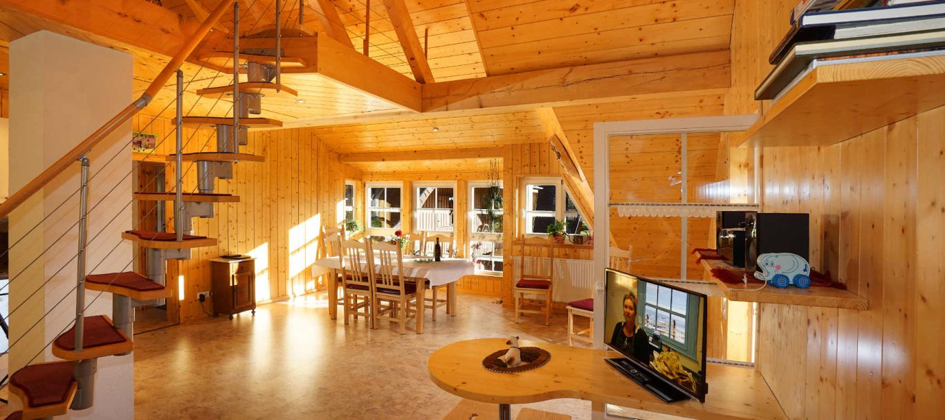 Ferienwohnung Blumenwiese Gemütliches, modernes Holzhaus mit offenem Wohnraum, Treppe und großen Fenstern.