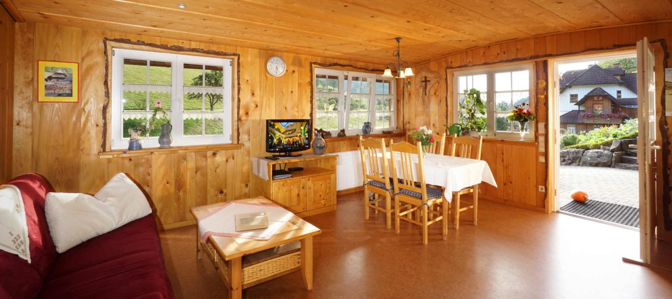 Ferienwohnung Obstgarten Gemütlicher Holzraum mit Tisch, Stühlen, Sofa und Blick auf die Landschaft.